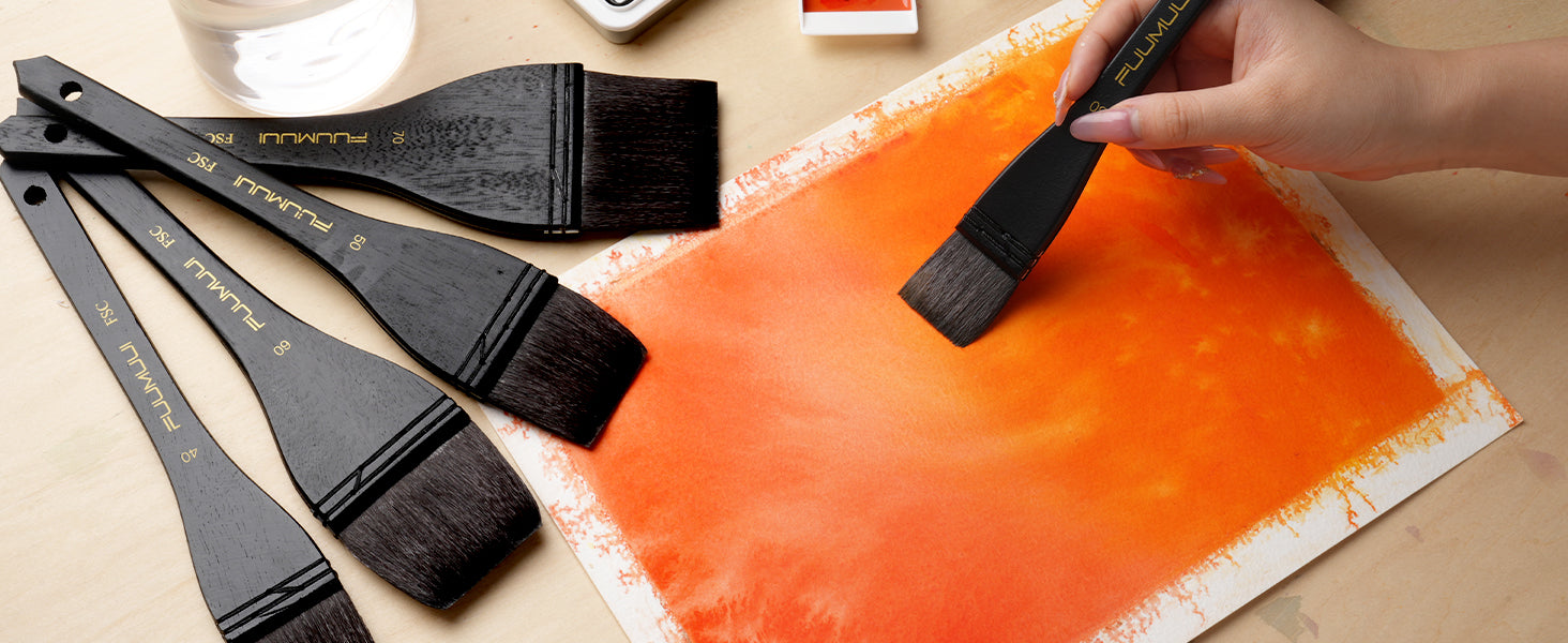 Professional artist using a FUUMUUI Squirrel Hair wash brush to apply orange watercolor paint on Cold Press paper. Set of wide flat brushes in sizes 40, 50, 60, and 70 with FSC-certified wooden handles.