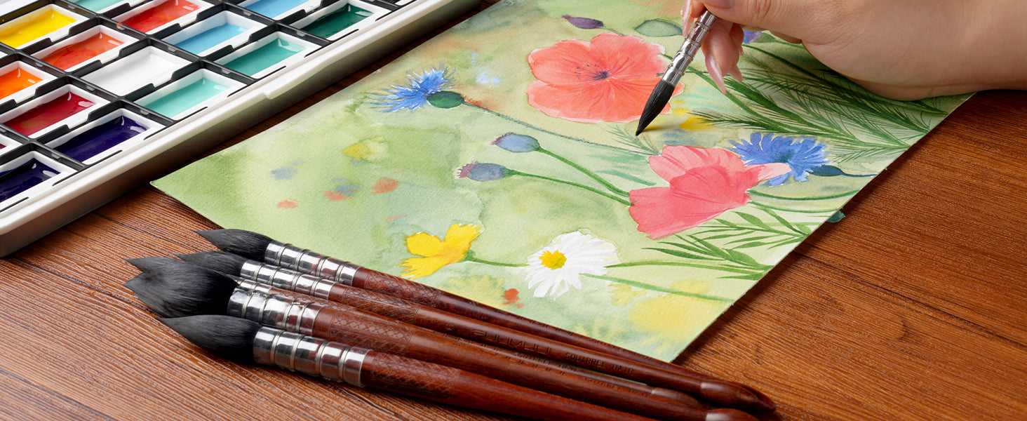Professional artist using a Fuumuui Squirrel Hair Watercolor Brush to paint floral art on cold press paper. High-quality mop brushes shown with a vibrant watercolor paint set and pigment pans on a wooden table.