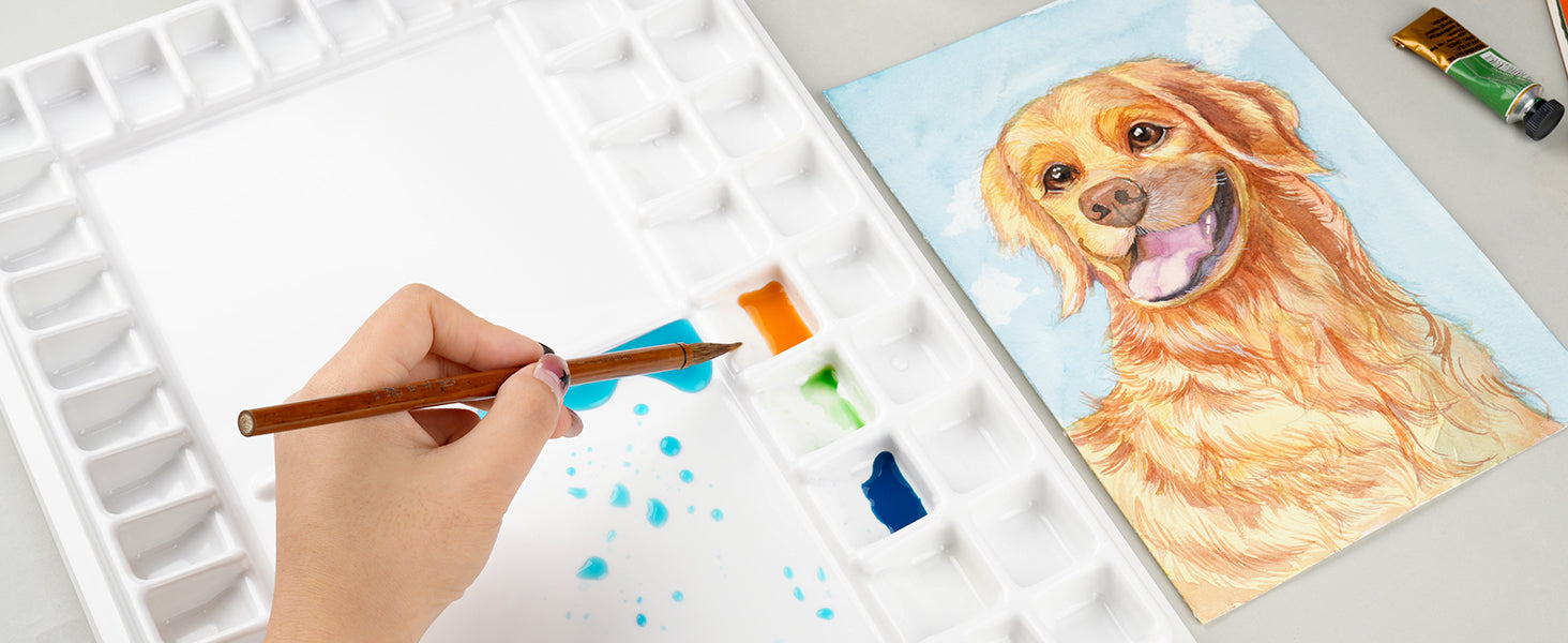 Artist using a Kolinsky Sable watercolor brush to mix blue pigment on a large white palette. A golden retriever pet portrait is painted on 140lb cold press 100% cotton watercolor paper.
