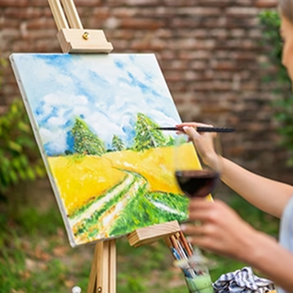 A person using a Fuumuui portable squirrel hair travel brush to paint a landscape on an easel outdoors.