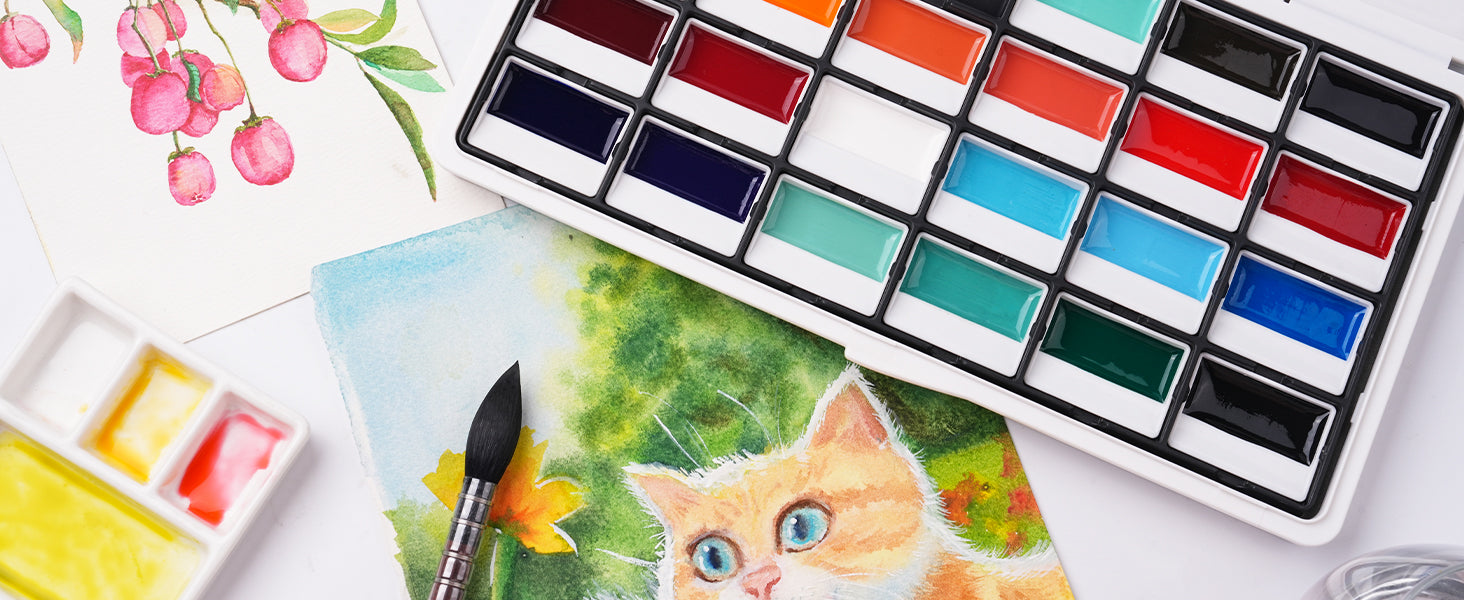 Vibrant watercolor paint set with multiple pans next to a pointed squirrel hair watercolor brush, small plastic palette, and a colorful cat painting on textured cold press watercolor paper.