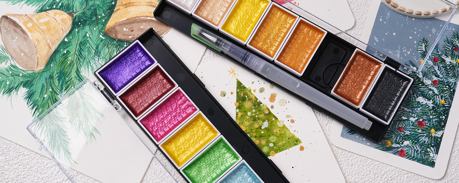 Shimmering metallic watercolor paint set with high-pigment pans and a synthetic travel water brush on cold press watercolor paper. Ideal for professional artists and beginners creating festive holiday greeting cards.