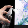 Fuumuui Pressureless Spray Bottle held in hand, spraying a fine mist from the clear bottle, against a vibrant floral watercolor background.