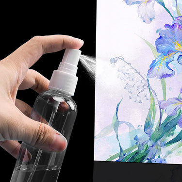 Fuumuui Pressureless Spray Bottle held in hand, spraying a fine mist from the clear bottle, against a vibrant floral watercolor background.