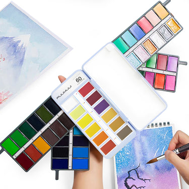 Set di pittura ad acquerello a 60 colori Fuumuui aperto, che mostra la sua gamma completa di colori vivaci su tavolozze compatte, con un artista che dipinge arte ad acquerello.