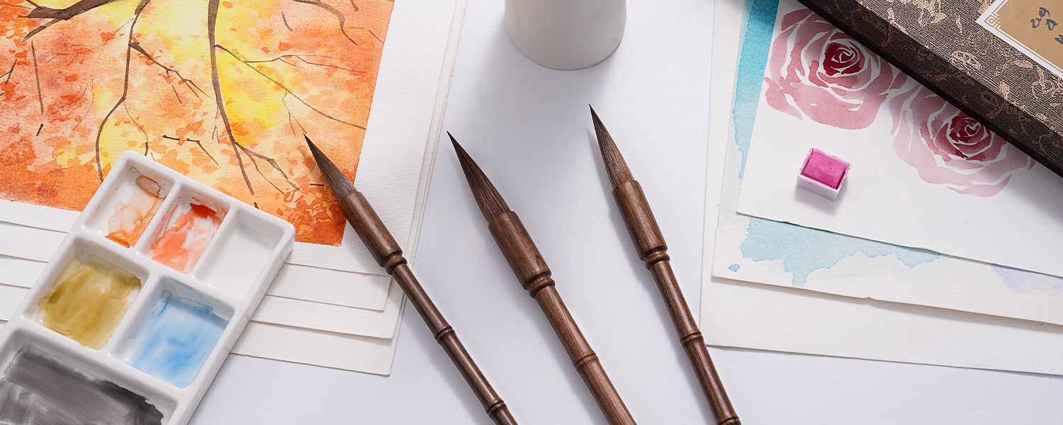 Professional Chinese Calligraphy Brushes with wooden handles on cold press watercolor paper, featuring a white ceramic palette and vibrant paint pans for professional artists and beginners.