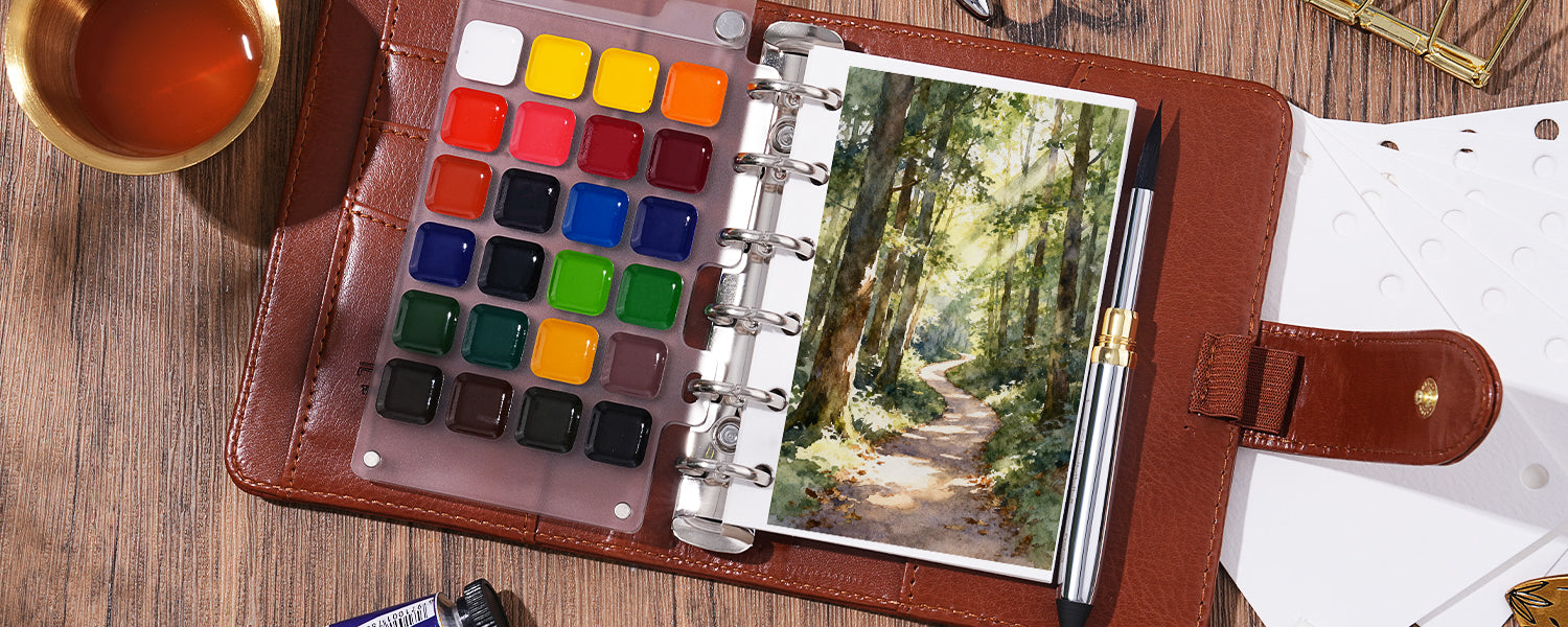 Travel watercolor paint set with a clear travel palette and squirrel hair travel watercolor brush in a leather sketchbook, featuring a forest scene on cold press watercolor paper for professional artists.