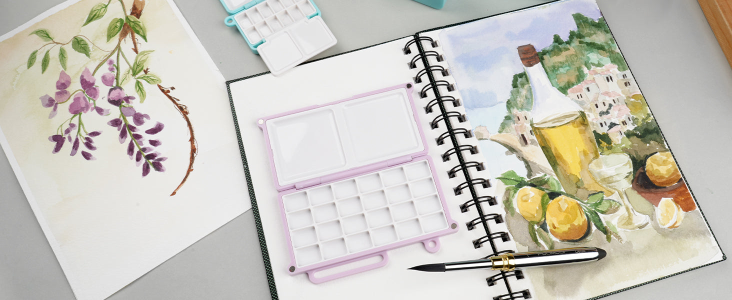 Fuumuui travel pocket brush and purple travel palette on a spiral-bound sketchbook with watercolor paintings on textured cold press paper. Portable art supplies for professional artists and beginners.