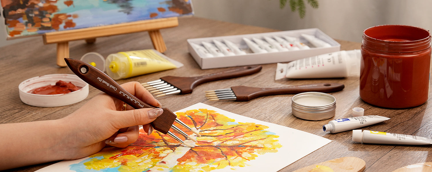 Professional artist using a Fuumuui Comb Brush Flat with synthetic nylon bristles to create texture with acrylic paint. Professional art supplies including acrylic paint tubes and more comb brushes on a wooden desk.