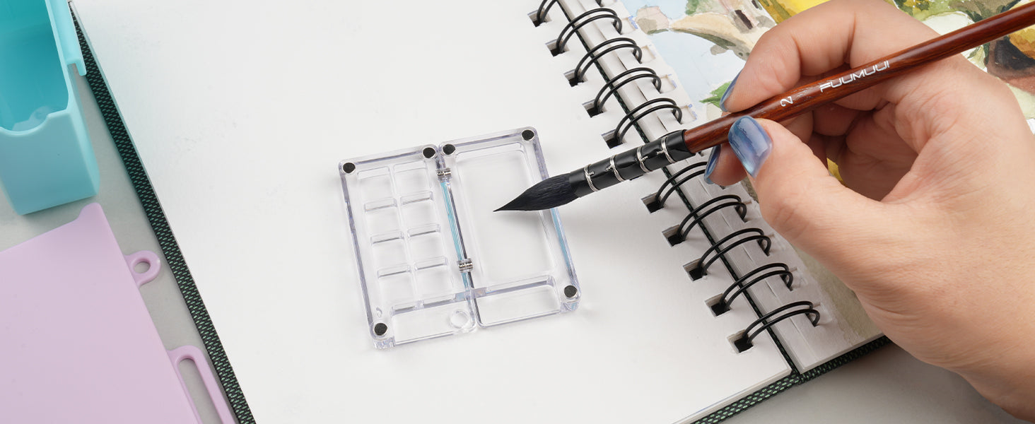 Size 2 Fuumuui squirrel hair watercolor brush dipping into a clear plastic travel palette over a spiral-bound watercolor sketchbook with cold press paper, perfect for professional artists and beginners.