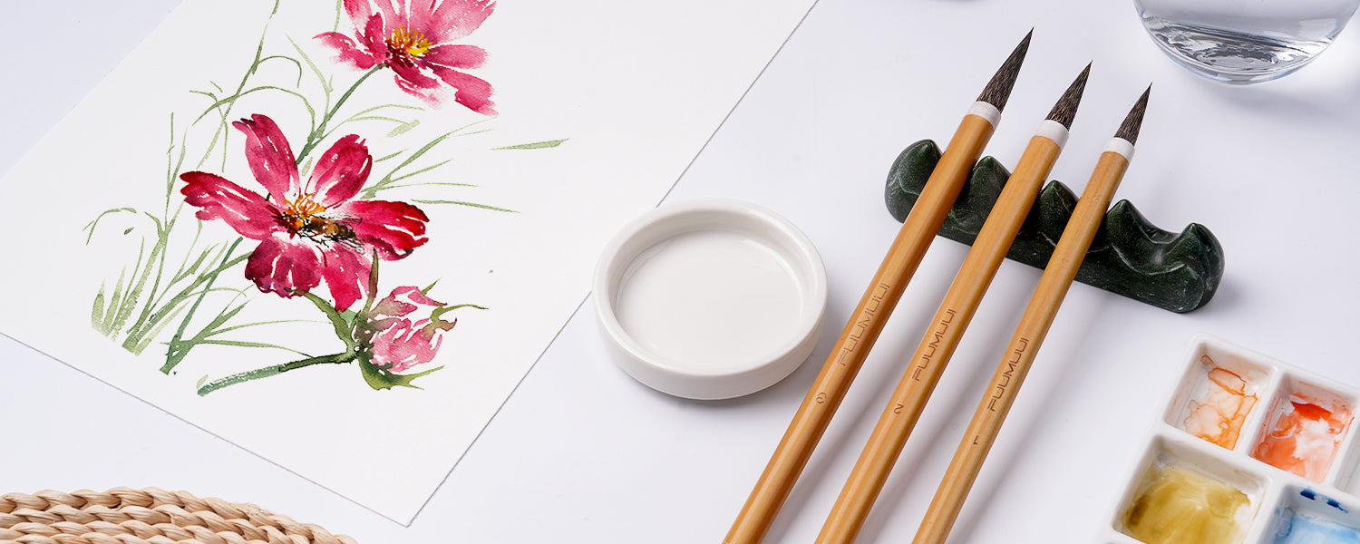 Fuumuui Chinese Calligraphy Brush set with squirrel hair tips in sizes 1, 2, and 3. Professional watercolor brushes on a stone rest next to a white ceramic palette and pink floral art on textured cold press paper.