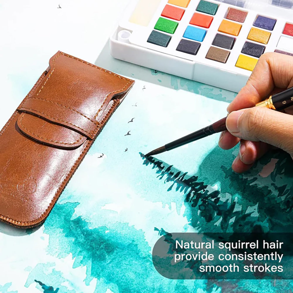 An artist using a Fuumuui natural squirrel hair watercolor brush for smooth strokes on paper, next to a paint palette and leather case.
