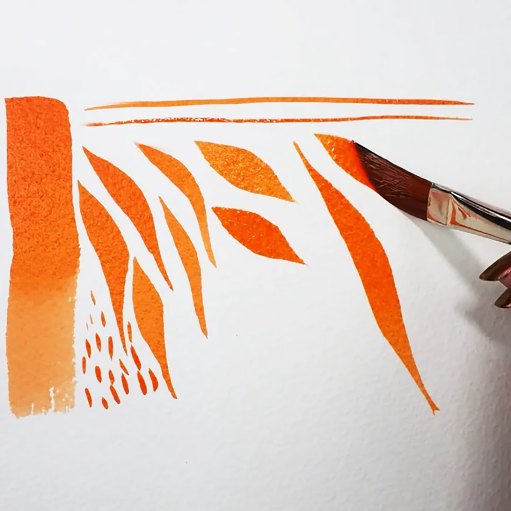 A sable watercolor brush painting different orange strokes, including foliage and broad washes.