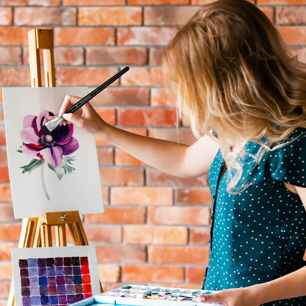 A female artist using a Fuumuui professional squirrel hair watercolor brush to paint a large purple flower on a canvas.