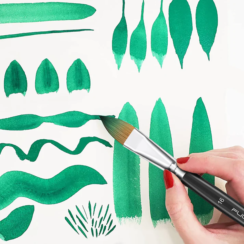 A hand holding a sable watercolor brush creating different green strokes and leaf shapes on white paper.