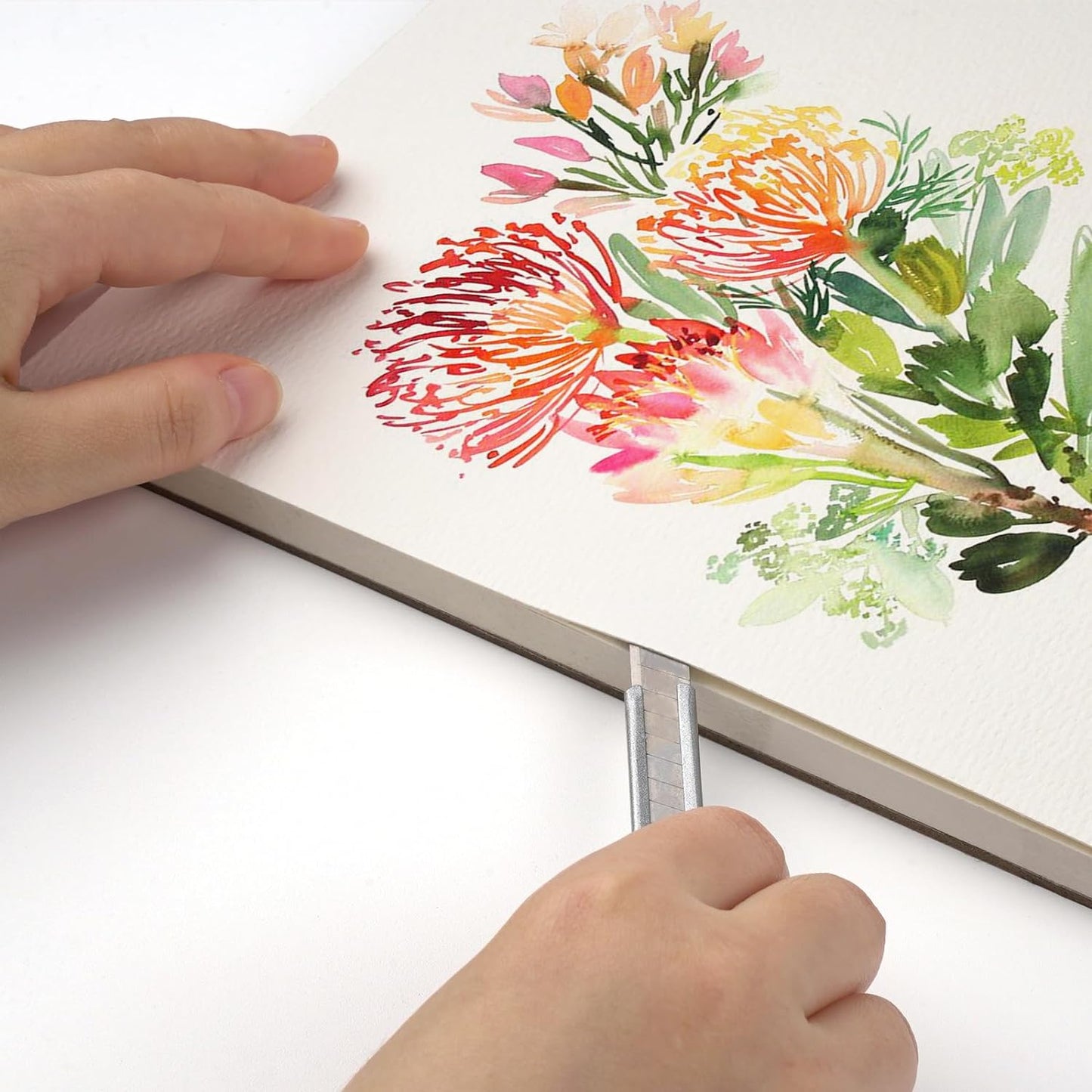 A hand cutting a finished watercolor floral painting from the watercolor paper pad.