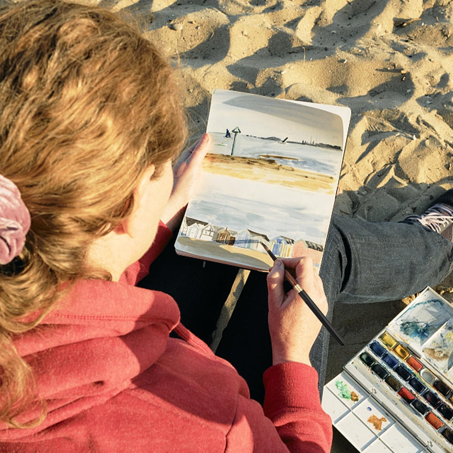 A person painting outdoors on the beach using a Fuumuui travel watercolor brush and paper pad.