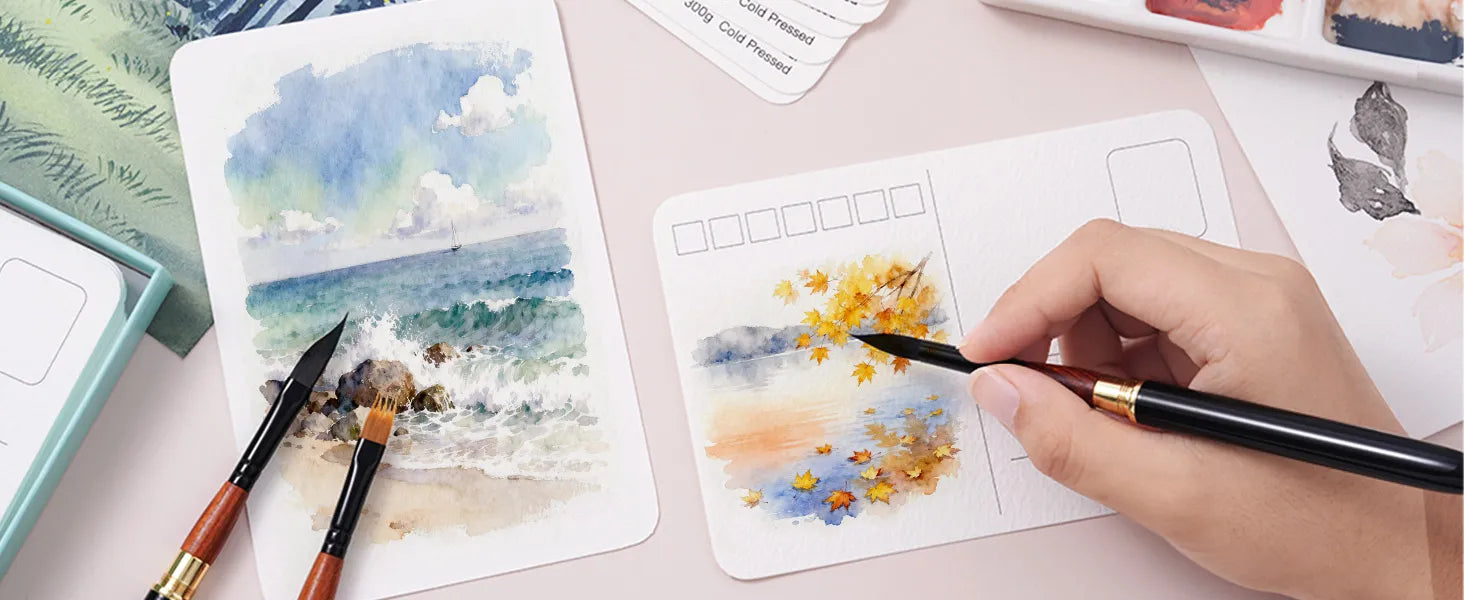 Artist painting on 100% Cotton 300gsm Cold Press Watercolor Postcards. 4x6 inch 40 sheets of textured paper shown with professional watercolor brushes, landscape art, and a paint palette.