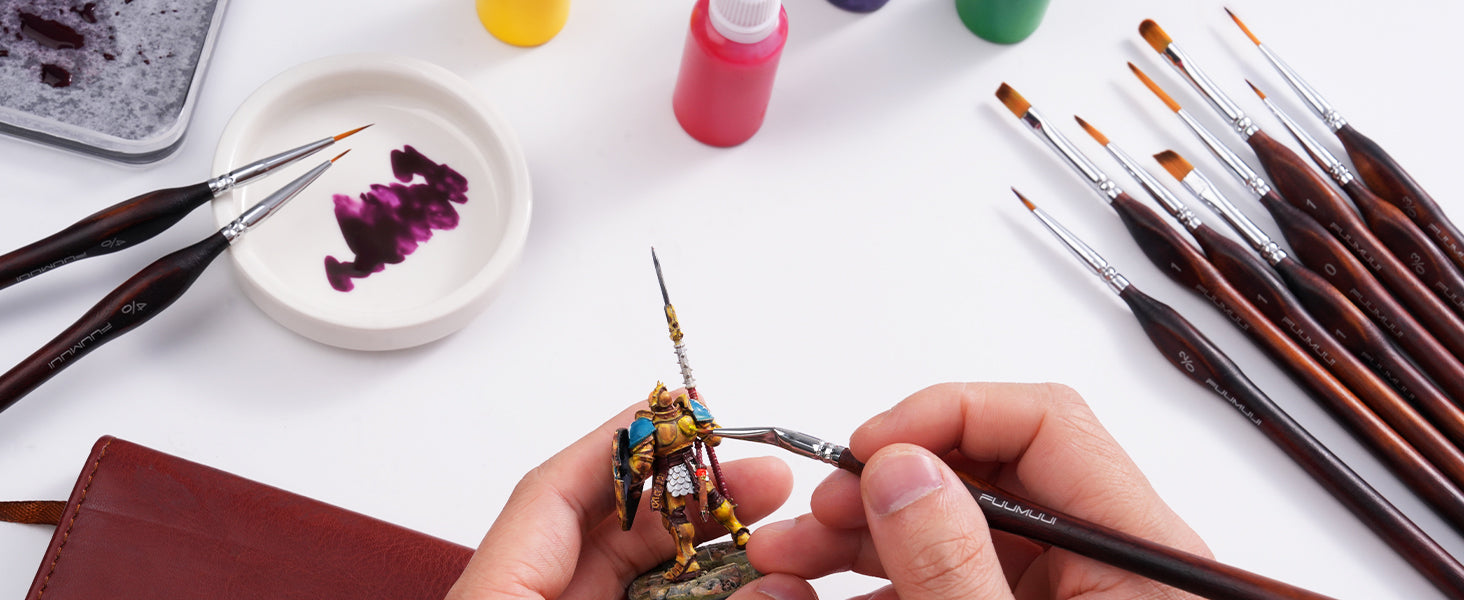 Professional artist using a Fuumuui Synthetic Nylon Miniature Paint Brush to paint a figurine. 11pcs Professional Nylon Detail Brushes set in 7 shapes, including sizes 4/0 and 2/0, ceramic palette, and acrylic paint.