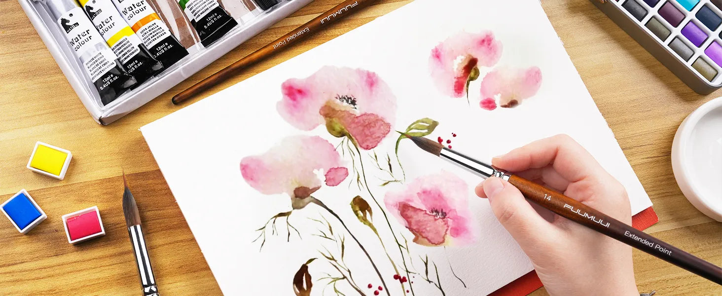 Professional artist using a Fuumuui size 14 Kolinsky Sable Extended Point Watercolor Brush on cold press paper. Includes watercolor paint tubes, half pans, and a travel palette for detailed floral painting.
