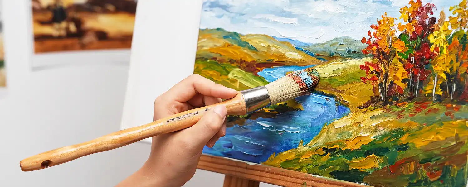 Hand holding a long handle hog bristle brush to paint a colorful oil landscape canvas with textured strokes.