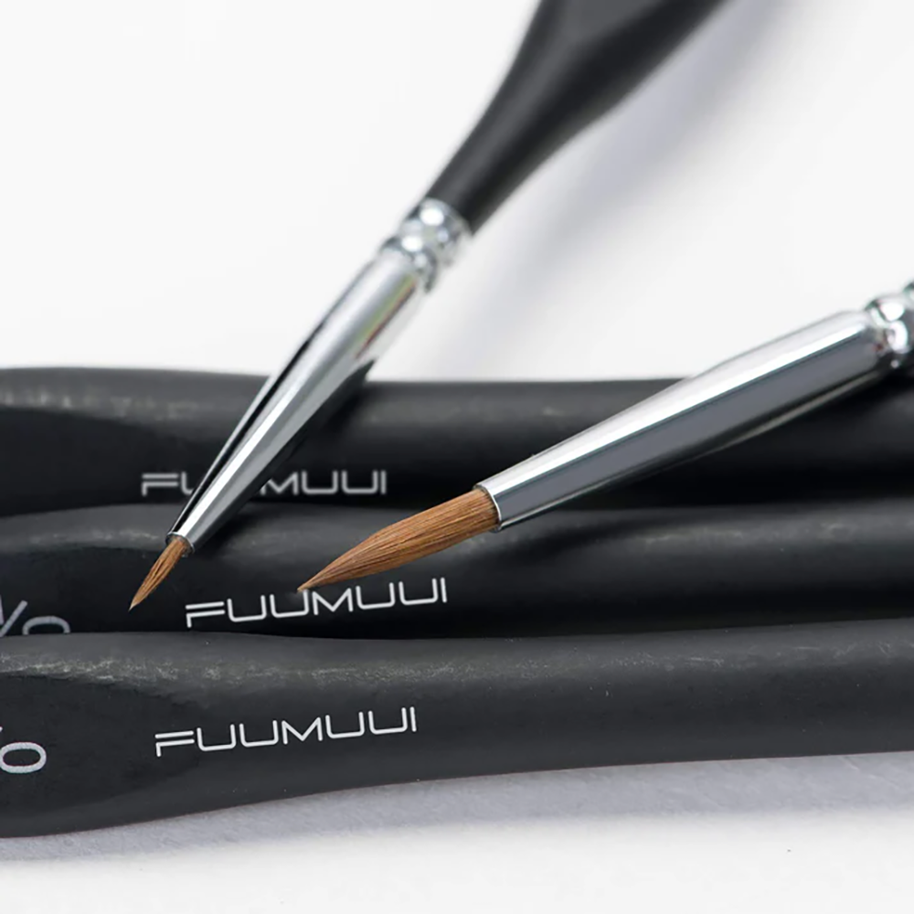 A close-up shot of two professional sable detail brushes showing their fine sable hair tips and ergonomic handles, perfect for miniature painting.