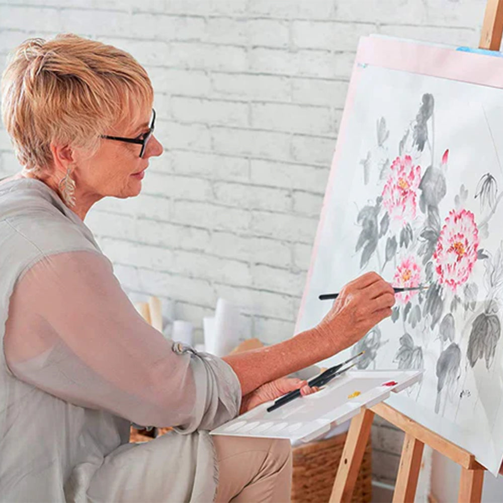 An artist works on a large painting of flowers using professional sable brushes and a palette, demonstrating the use of high-quality detail brushes for delicate work.