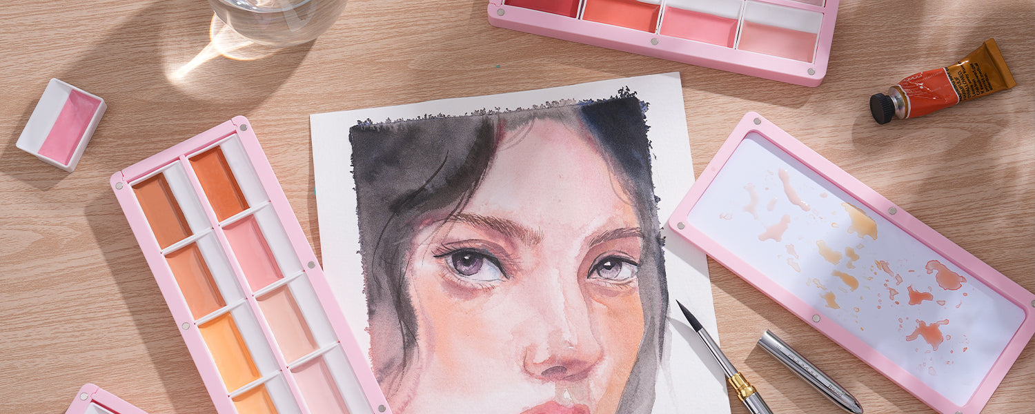 A watercolor portrait painting surrounded by FUUMUUI 3-Tier Light Pink Magnetic Palettes, tube paints, and brushes.