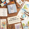 Fuumuui 6.3 inch square cotton watercolor sketchbook surrounded by art supplies and mixed media drawings.