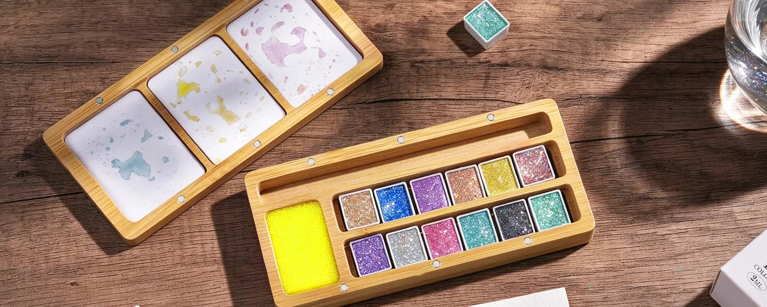 Fuumuui 12 shimmer watercolor paint set opened on wooden desk with ceramic palette and half pans.