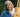 Professional artist Annie Strack holding a fine-tip watercolor brush next to a wooden easel with a Fredrix canvas panel. Ideal for professional artists and beginners using watercolor paint and acrylic paint.