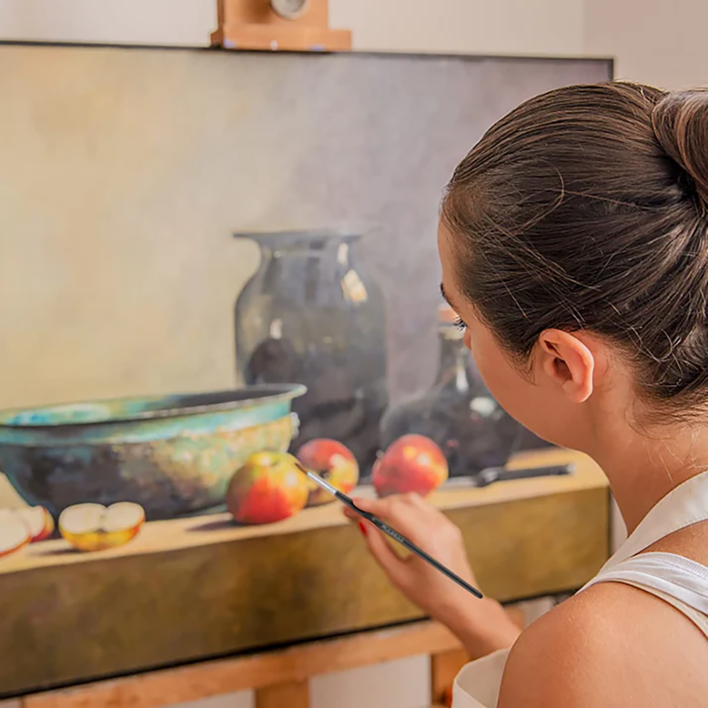 An artist using a Fuumuui professional watercolor brush to paint a still life with apples and a vase.
