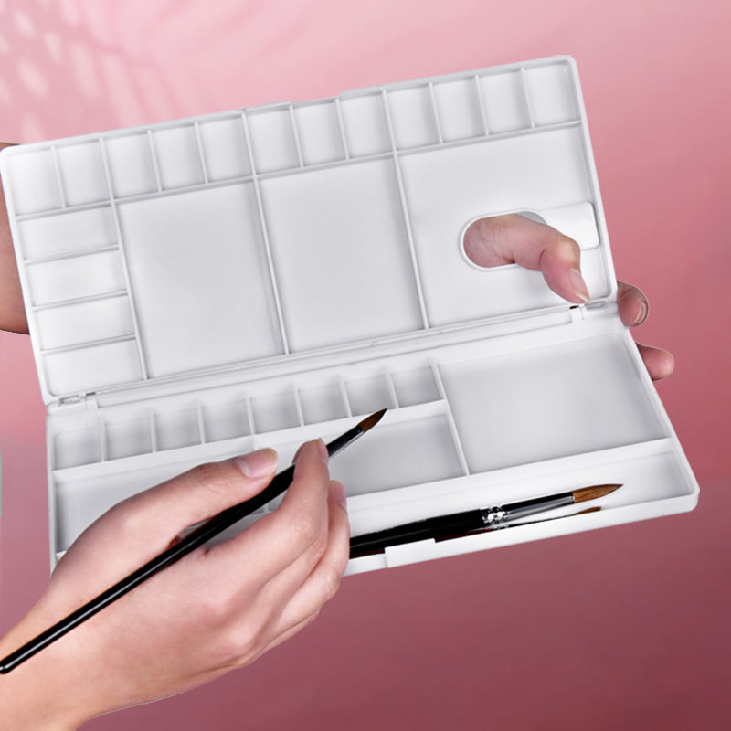 A white Fuumuui watercolor palette with an attached lid that helps keep paints moist for painting projects.