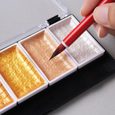 Colori ad acquerello metallici ad alte prestazioni FUUMUUI: il pennello dell'artista si immerge nell'oro rosa scintillante, con godet oro e argento.