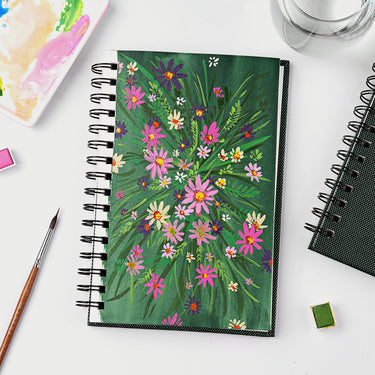 Fuumuui Watercolor Sketchbook, spiral bound with 100% cotton paper, displaying a vibrant floral watercolor painting, surrounded by Fuumuui art supplies including a brush and palette.