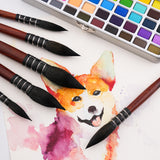 Pennelli professionali per acquerello Fuumuui da 6 pezzi con setole scure e manici in legno, disposti attorno a un dipinto ad acquerello di un cane felice, accanto a una tavolozza per acquerello.