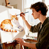 Una giovane artista dipinge un vivace ritratto di un gatto arancione e bianco usando un pennello filbert sintetico a doppio strato Fuumuui del loro set di forniture artistiche Fuumuui, ideale per tecniche ad acquerello e acrilico.