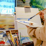 Fuumuui professioneller flacher Nylonhaar Acrylpinsel malt einen blauen Horizont auf Leinwand; Künstler hält eine Palette, andere Kunstpinsel in der Nähe.