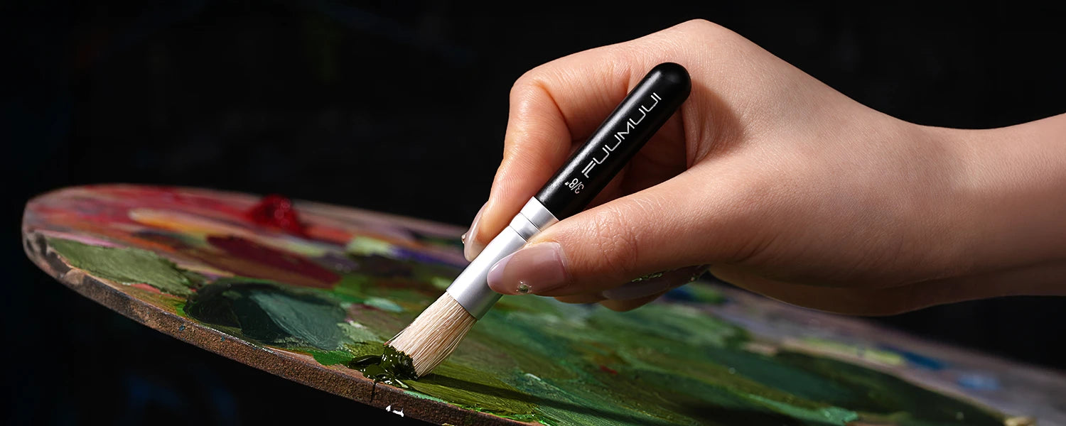 Artist using a Fuumuui 3/8 inch natural bristle oil paint brush to mix green pigment on a wooden palette. Versatile acrylic paint brush with stiff bristles for professional artists and beginners.