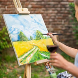 Artista che utilizza il set di 3 pennelli da viaggio professionali in pelo di scoiattolo Fuumuui per dipingere un paesaggio all'aperto su un cavalletto.