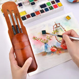 Set di 4 pennelli da viaggio in martora Fuumuui in una custodia protettiva marrone, con un pennello utilizzato per dipingere una vivace scena ad acquerello.