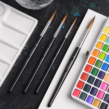 Pinceaux d'aquarelle Fuumuui Ultimate Kolinsky Collection (tailles individuelles) offrant précision, ressort et contrôle, présentés avec une palette de peinture vibrante et un plateau de mélange.