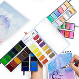 Set di pittura ad acquerello a 60 colori Fuumuui aperto, che mostra la sua gamma completa di colori vivaci su tavolozze compatte, con un artista che dipinge arte ad acquerello.