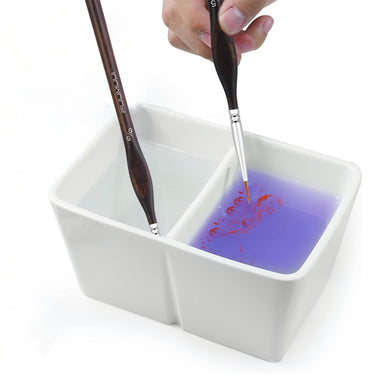 Fuumuui Keramik-Pinselwaschbecken mit zwei geteilten Fächern, mit einem Pinsel, der in sauberem Wasser einweicht, und einem anderen, der rote Farbe in lila Wasser spült.
