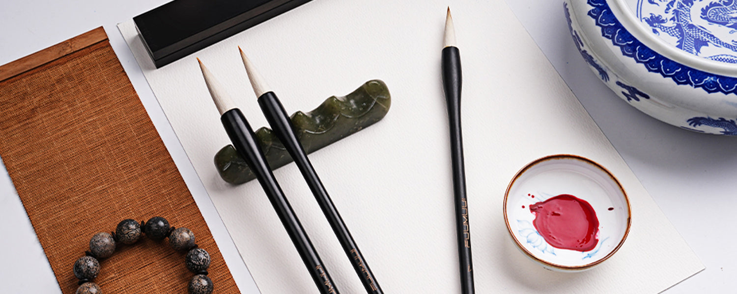 Three Fuumuui Chinese Calligraphy Brushes on Cold Press watercolor paper with a jade brush rest and ceramic palette of red pigment, perfect for professional artists practicing traditional painting and detail work.