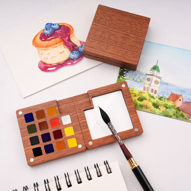Set di acquerelli in legno premium Fuumuui con 15 colori selezionati a mano, una tavolozza di miscelazione integrata e un pennello per acquerello, esposto accanto a opere d'arte ad acquerello finite. Forniture artistiche Fuumuui di qualit¨¤ per artisti.