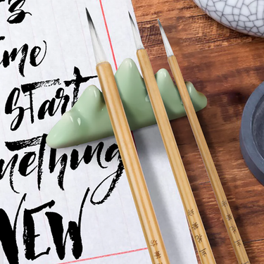 Fuumuui Chinese Calligraphy Wolf Sheep Mix Brushes on a green mountain-shaped rest, with ink stone and paper.