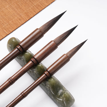 Fuumuui professional calligraphy brushes with dark bamboo section handles, suitable for watercolor, resting on a green jade brush rest.