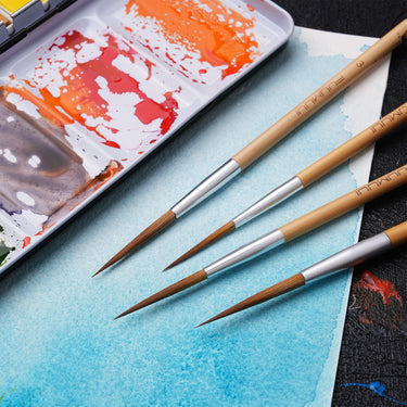 Fuumuui Fournitures d'art : Ensemble de 4 pinceaux à pointe longue en poils d'animaux pour aquarelle et calligraphie avec manches en bambou, présentés sur du papier aquarelle bleu à côté d'une palette de peinture.