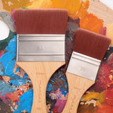 Fuumuui 2pcs Large Nylon Flat Brushes (80mm and 50mm) with wooden handles and brown synthetic bristles, lying on a colorful artist's palette filled with paint for Watercolor, Acrylic & Oil Painting.